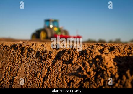 Close up of tilled soil with tractor diffused in background Stock Photo