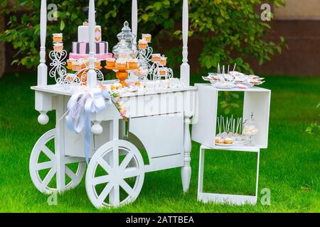 Candy Bar. White wooden trolley with sweets on green grass in the garden Stock Photo