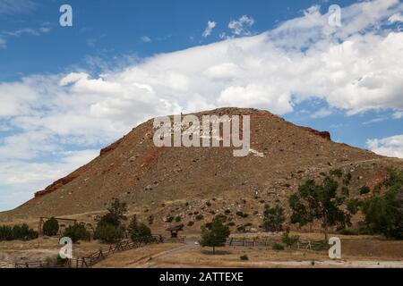 A large mound or hill with rocks painted in white saying it is the Worlds Largest Mineral Hot Springs in Termopolis, Wyoming. Stock Photo