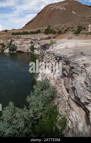 Travertine and gypsum layers left from many years of hot mineral water flow now form an embankment along the Bighorn River in Thermopolis, Wyoming. Stock Photo