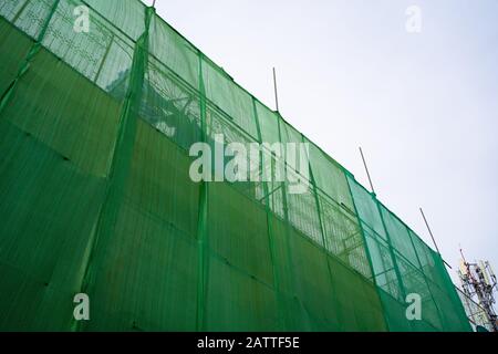 Construction building wrapped with green fabric for safety reasons Stock Photo