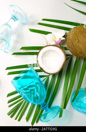 Coconut summertime entertaining theme flat lay creative layout overhead with shadows from blue drinking glasses cast over table. Vertical close up. Stock Photo