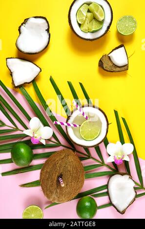 Coconut summertime entertaining theme flat lay creative layout overhead with coconuts filled with summer drinks and cocktails on modern pink and yello Stock Photo
