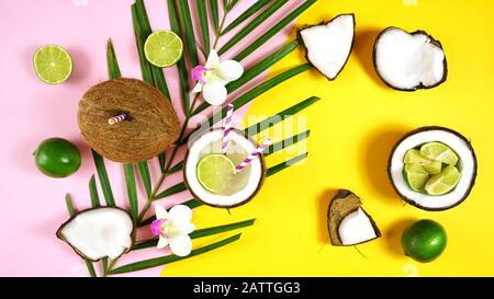 Coconut summertime entertaining theme flat lay creative layout overhead with coconuts filled with summer drinks and cocktails on modern pink and yello Stock Photo