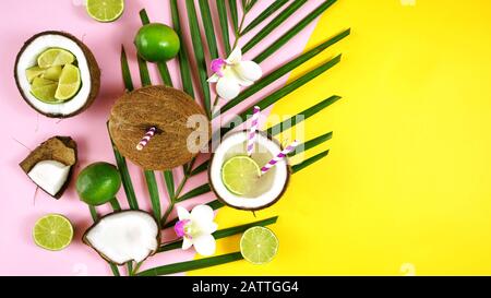 Coconut summertime entertaining theme flat lay creative layout overhead with coconuts filled with summer drinks and cocktails on modern pink and yello Stock Photo