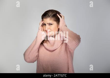 Close up portrait of a young Caucasian woman wearing a pink sweater on a grey background.  The model looks shocked and scared Stock Photo