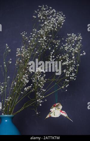 An origami hummingbird hanging from dried Gypsophila in a vase. Stock Photo