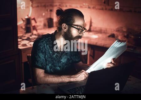 A hipster type young man checking billing information in the kitchen.Subsistence Concept. Stock Photo