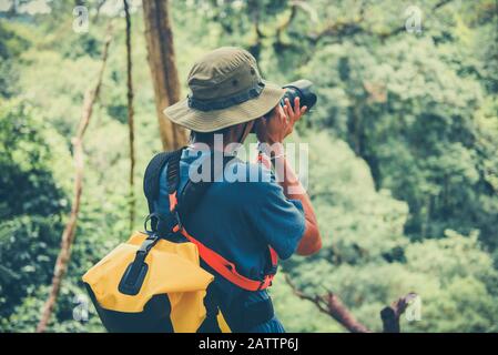 Outdoor adventure and Traveler man holding camera on nature forest tourist on holiday vacation trips adventurous backpacking travel hike / Man photogr Stock Photo