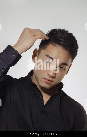 Handsome Asian man with short haircut posing in a trendy black hat and  black t-shirt against gray background in the studio. Indoor photo of a  confident guy in stylish black clothing looking