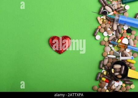 Frame made of pills and capsules put in line. Drugs near syrup bottle, syringes, heart and measuring spoon. Medicine and love concept. Set of colorful pills scattered on green background, copy space Stock Photo