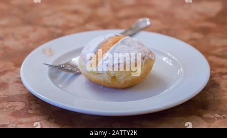 An original austrian Krapfen (also: Berliner, a kind of doughnut) served on a plate. A sweet speciality in german speaking countries. Stock Photo
