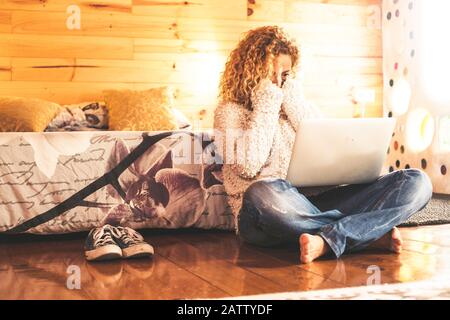 Surprised and scared caucasian woman looking a computer laptop monitor sit down on the wooden floor at home or hotel Stock Photo