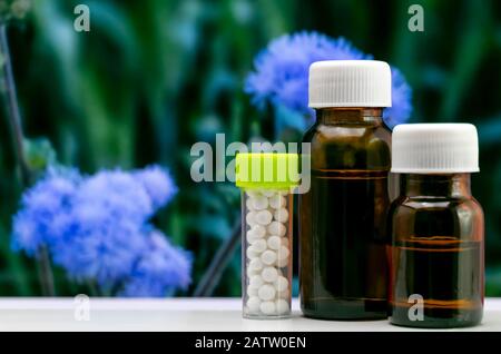 Advanced Homeopathic Concept - Close up image of homeopathic globule sugar pills and liquid substance in glass bottle with blurred blue flower and gre Stock Photo