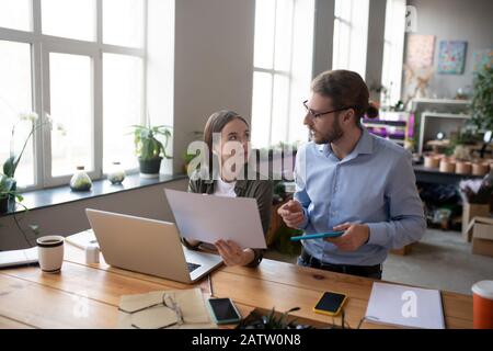Project discussion. Young man in glasses and with tablet in his hand, seriously looking and talking and a long-haired girl with project in his hand, l Stock Photo
