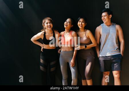 Happy smiling man and women having fun talking in gym. Group of young people relaxing in gym after workout training with black background. Stock Photo