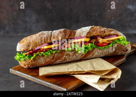 A sandwich of dark bread with salad, bacon, tomatoes, cheese and onions. Baguette. Breakfast. Fast food. Healthy eating. Recipes. Stock Photo