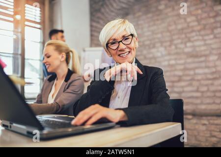 Senior and young colleagues women sitting in modern office using laptop. Stock Photo