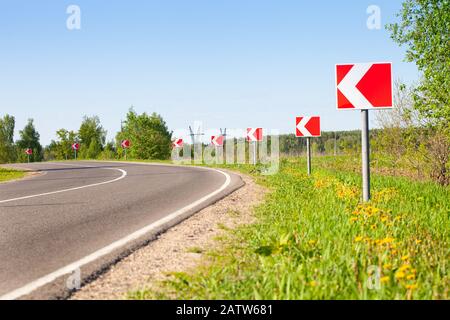 Asphalt road with bright traffic signs in situ of the sharp left turn Stock Photo