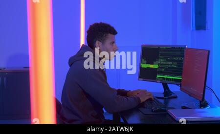 Profile view of african programr working in cyber security center in dark room. He typing something on keyboard. Stock Photo
