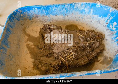 Clay, dirt with straw in barrow wheel. Cob, clom eco building construction techniques Stock Photo