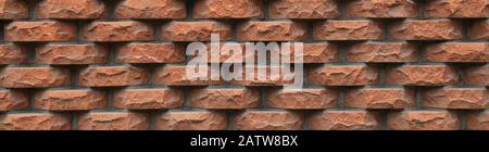Embossed brown-colored grungy brick wall, lined with separate rough and hewn bricks. The fragment of a new decorative bricklaying. Stylish design Stock Photo