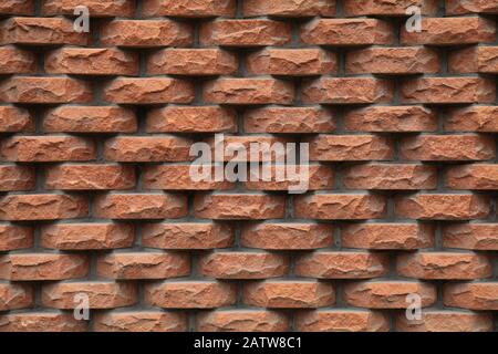 Embossed brown-colored grungy brick wall, lined with separate rough and hewn bricks. The fragment of a new decorative bricklaying. Stylish design Stock Photo