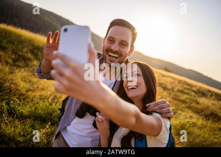 Happy couple is hiking in mountain. They are taking selfie. Stock Photo