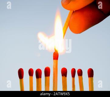 A person lighting a match stick with another match with fire holding in his hand over eight other matches Stock Photo