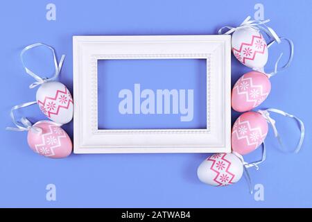 Easter design with blank white picture frame surrounded by simple pink and white easter eggs on pastel violet background Stock Photo