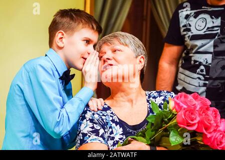 The boy whispers in his grandmother's ear and shares the news Stock Photo