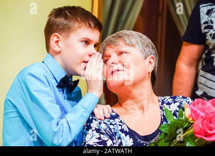 The boy whispers in his grandmother's ear and shares the news Stock Photo