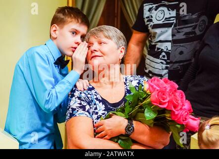 The boy whispers in his grandmother's ear and shares the news Stock Photo