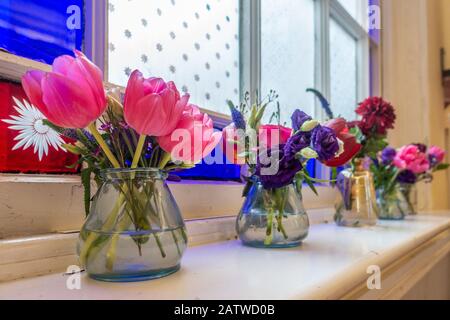 Cut flowers in glass vases on a window sill in front of a stained glass window Stock Photo