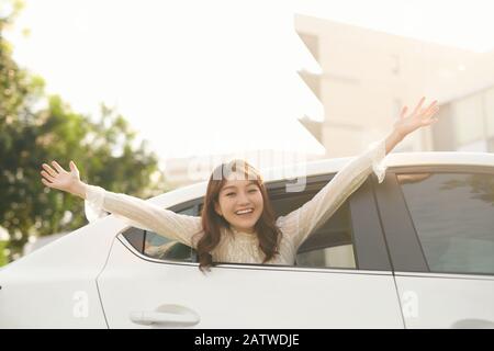 Happy Young Woman Raising Hand Out Of Car Window Stock Photo