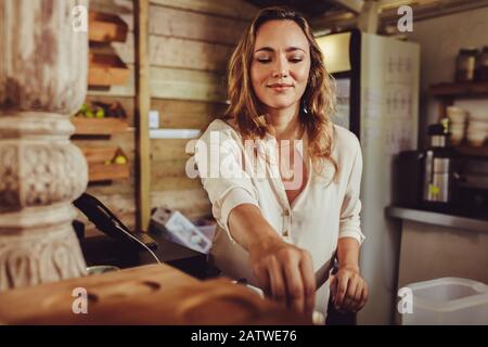 Woman working in a coffee shop. Young female barista standing behind the bar in cafe and working. Stock Photo
