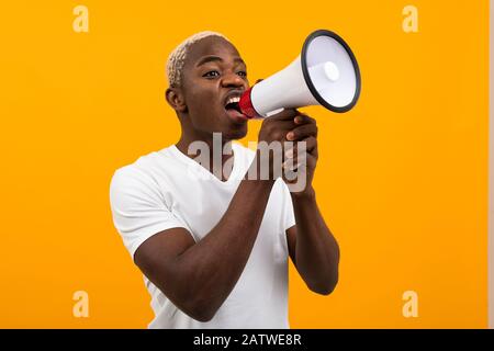 black american man in white t-shirt tells the news through a megaphone on an isolated orange background Stock Photo