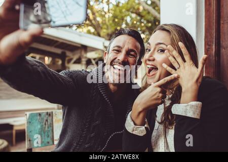 Affectionate couple announcing their engagement with selfies while sitting at cafe. Happy couple taking a selfie and showing off their wedding ring at Stock Photo