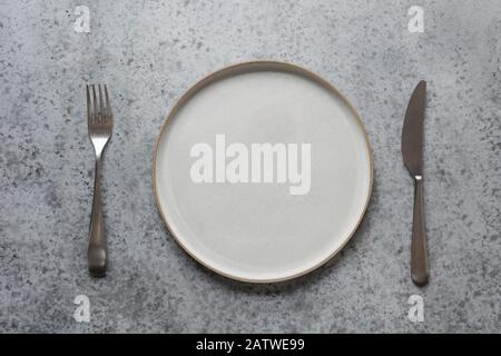 Empty modern modus plate, fork and knife on grey stone table. Minimal table place setting. Space for text or menu. View from above. Stock Photo