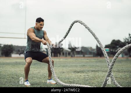 Man doing fitness workout outdoors. Fit young man doing workout using two battle ropes on the ground. Stock Photo