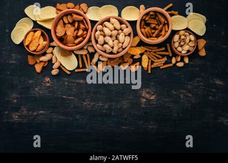 Snack for beer. Salted crackers, chips, nuts, peanuts, pistachios. On a wooden background. Free space for text. Top view. Stock Photo