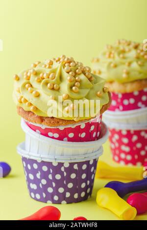 Funny cupcakes in funny polka dot   cups and deflated balloons on yellow background, close up, copy space Stock Photo