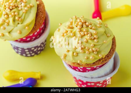 Funny cupcakes in funny polka dot   cups and deflated balloons on yellow background, close up, copy space Stock Photo