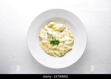 Dumpling from potatoes under cheese sauce. On a wooden background. Top view. Free space. Stock Photo