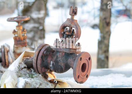 Old, rusty shut-off valve on a heating pipe on a winter background. Stock Photo