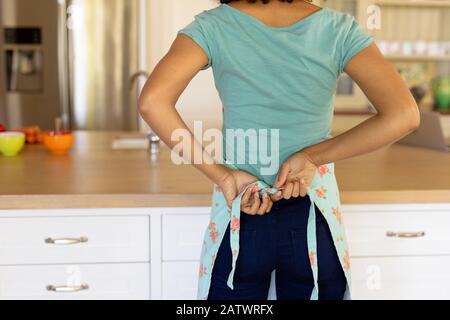 Young woman wearing apron cooking and rolling dough with pin in kitchen