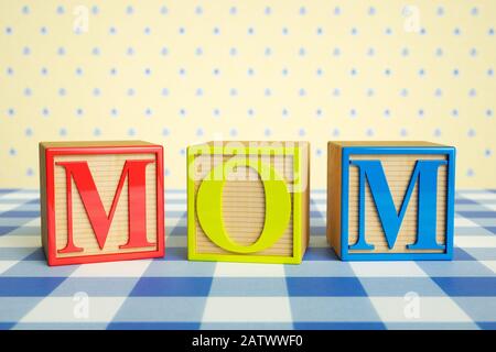 Childrens wooden ABC blocks spelling MOM on a checked tablecloth Stock Photo