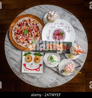 Restaurant food. A table with delicious and interesting desserts for children. Ice Cream, Cocktails and Blisters on the Plates. Cheerful food. Stock Photo