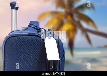 Blue suitcase with empty paper label closeup on the background of tropical beach Stock Photo