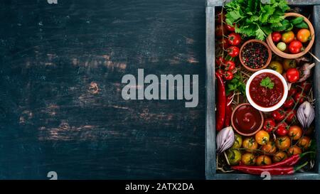 Assortment of tomato sauces in a wooden box. Ketchup. Cherry tomatoes, spices, chili peppers, olive oil, parsley. Top view. Stock Photo
